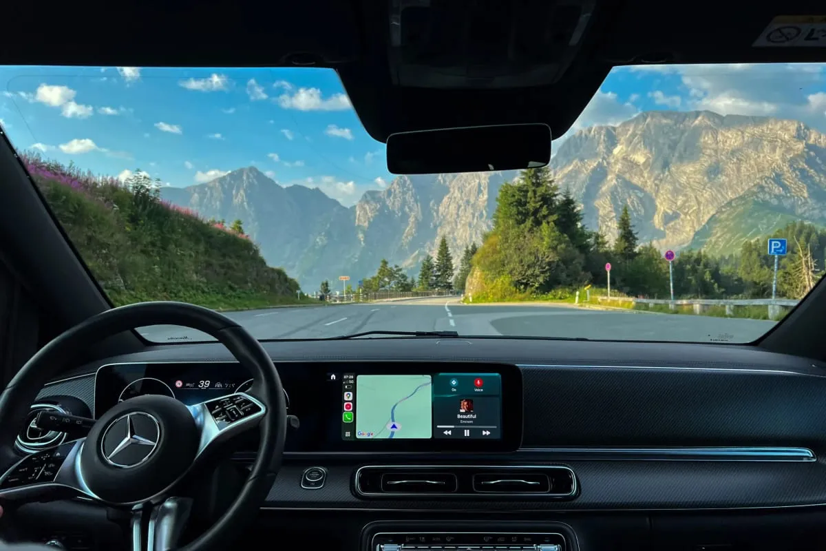 Blick aus dem Fahrzeug über Lenkrad und Navigationsdisplay auf eine kurvige Alpenstraße